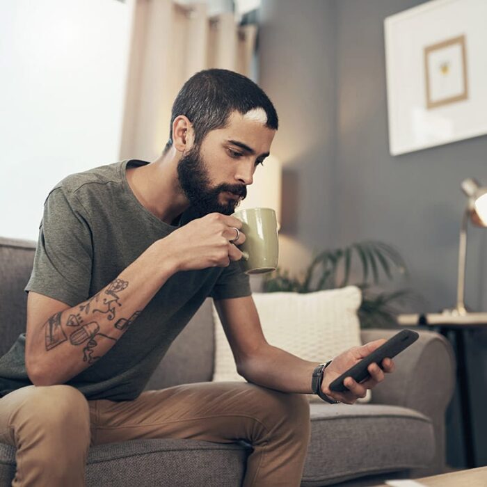 a man sitting on a couch drinking coffee and using a phone