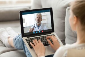 woman on couch talks to an online doctor on her laptop