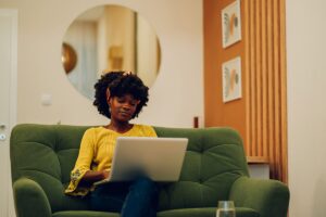 a woman sitting on a green couch using a laptop