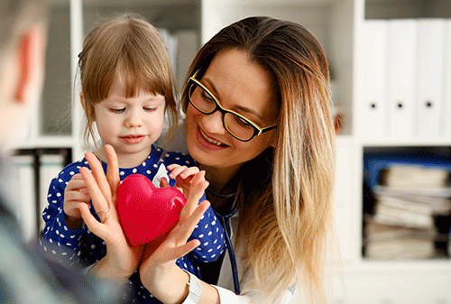 a pediatric cardiologist holds a toy heart with a child